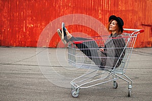 Fashion hipster cool girl in shopping cart having fun against th