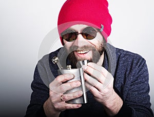 Fashion hipster cool man in sunglasses and colorful clothes pours himself a drink from a metal flask