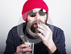 Fashion hipster cool man in sunglasses and colorful clothes pours himself a drink from a metal flask