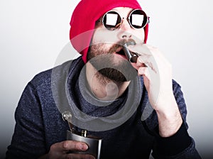 Fashion hipster cool man in sunglasses and colorful clothes pours himself a drink from a metal flask