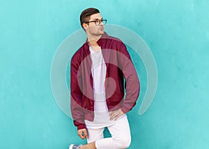 Fashion hipster guy in glasses poses near the wall the color of