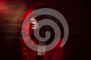 Fashion image of young woman with makeup and hairstyle, wear red suit, with closed eyes, red neon studio light.