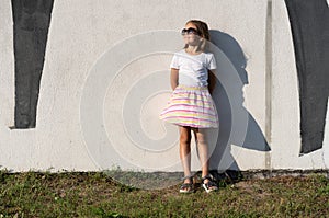 Fashion kid concept - stylish girl child wearing bright clothes and sunglasses against the white wall.