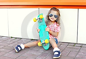 Fashion kid concept - stylish little girl child with skateboard wearing sunglasses in city