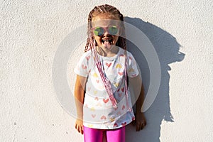 Fashion kid concept - stylish little girl child wearing bright clothes and sunglasses against the white wall.