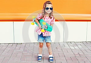 Fashion kid - stylish little girl child with skateboard wearing sunglasses in city