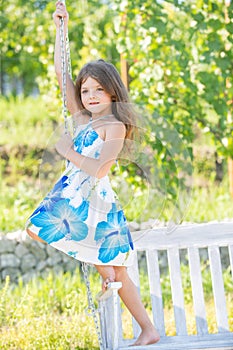 Fashion kids dress. Happy little child girl on a swing in the summer park. Dreamy kids face. Little child girl is