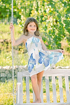 Fashion kids dress. Little child girl is swinging on a swing in summer park. Sunny joyful summer day. Child girl having