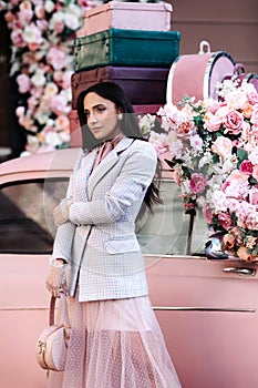 Fashion lady model in pink jacket skirt, makeup and black hair over retro car decorated with roses