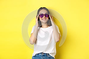 Fashion and lifestyle concept. Stylish asian woman trying new sunglasses in heart-shape, going on vacation, smiling