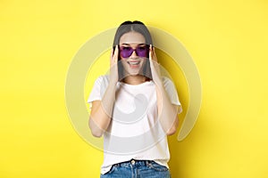 Fashion and lifestyle concept. Stylish asian woman trying new sunglasses in heart-shape, going on vacation, smiling