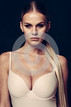 Fashion and lingerie concept - beautiful blond lady portrait in sexy nude color corset on black background. Woman