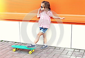 Fashion little girl child with skateboard wearing a sunglasses in city