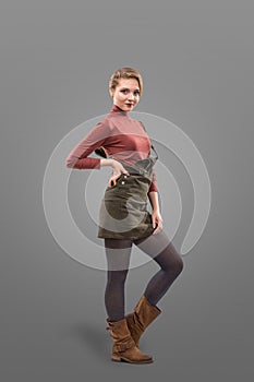 Fashion look of girl dressed in casual style in short skirt and broun boots isolated on grey background