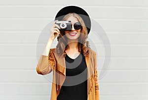 Fashion look, pretty cool young woman model with retro film camera wearing a elegant hat, brown jacket, curly hair outdoors