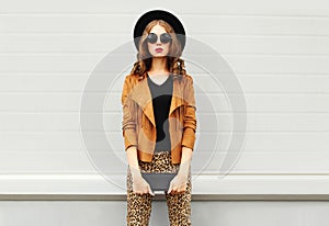 Fashion look, pretty woman wearing a retro elegant hat, sunglasses, brown jacket and black handbag clutch