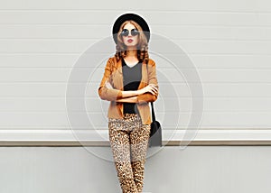 Fashion look, pretty young woman wearing a retro elegant hat, sunglasses, brown jacket and black handbag clutch