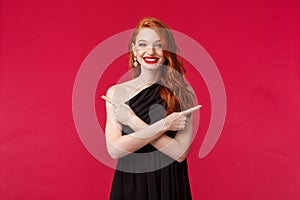 Fashion, luxury and beauty concept. Portrait of smiling redhead woman wearing makeup and black dress, pointing sideways