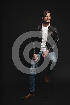 Fashion man, Handsome serious beauty male model portrait wear leather jacket, young guy over black background.