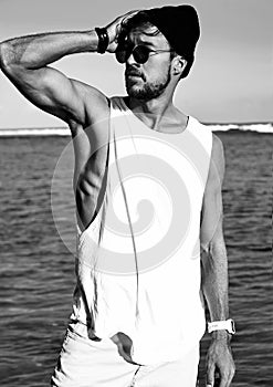 Fashion man model wearing casual clothes in black T-shirt and sunglasses posing on blue sky and ocean background