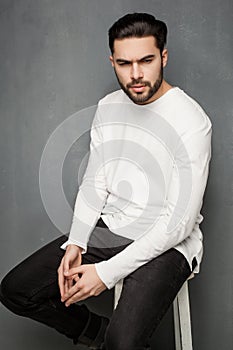 fashion man model in white sweater, jeans and boots posing dramatic