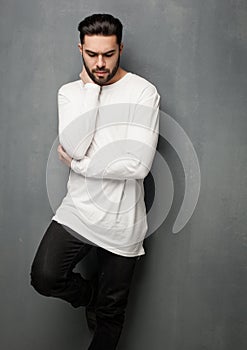 fashion man model in white sweater, jeans and boots posing dramatic