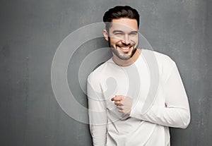 fashion man model in white sweater, jeans and boots smiling against wall