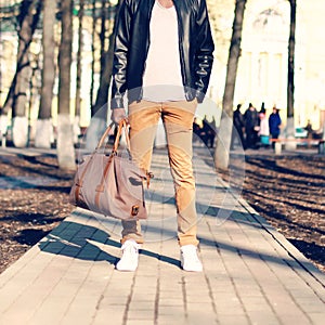 Fashion man stands with a bag in his hand outdoors closeup