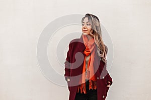 Fashion model attractive young woman in elegant stylish burgundy coat with orange bright fashionable scarf stands near vintage