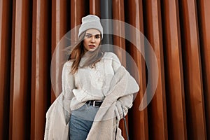 Fashion model of an attractive young woman in fashionable spring warm clothes in a knitted stylish hat posing and looking at the