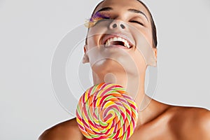 Fashion model with bird feather eyelashes smiles and holds a rainbow lollipop