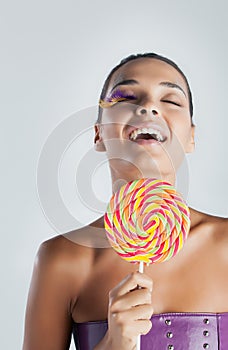 Fashion model with bird feather eyelashes smiles and holds a rainbow lollipop