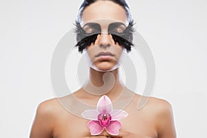 Fashion model with bird feather false eyelashes holds a lotus flower bold makeup