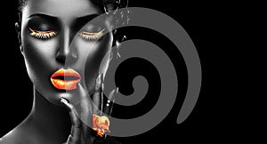 Fashion model with black skin, golden lips, eyelashes and jewellery - golden ring on hand. on black background