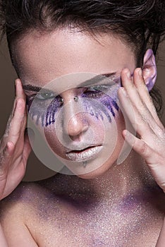 Fashion model with colorful make-up and blue glitter and sparkles on her face and body.