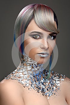 Fashion model with creative make-up and hairstyle. Foil, shiny shadows, glitter. Eyes, lips and colored hair coloring.