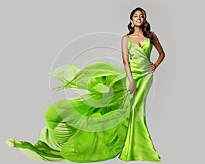 Fashion Model dancing in Green Silk Dress with Flying Chiffon Fabric. Beauty Woman in Long Satin Evening Gown over White. Elegant