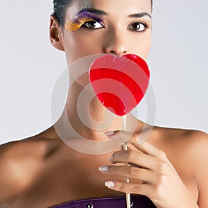 Fashion model with false feather eyelashes holds a red heart-shaped lollipop