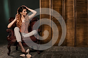 Fashion model in fashion clothing sitting in brown leather armchair posing in the studio.