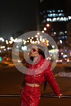 Fashion model girl with afri braid and red shiny skirt and winter coat standing outdoors in night city background. Night