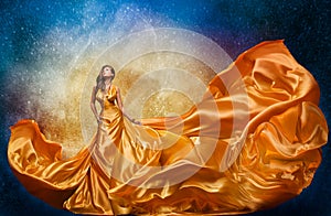 Fashion Model in Golden Dress over Miracle Night Sky Background. Luxury Woman in Long Silk Gown Dance and looking at Stars
