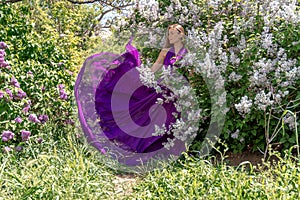 Fashion Model in Lilac Flowers, Young Woman in Beautiful Long Dress Waving on Wind, Outdoor Beauty Portrait in Blooming