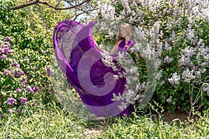 Fashion Model in Lilac Flowers, Young Woman in Beautiful Long Dress Waving on Wind, Outdoor Beauty Portrait in Blooming