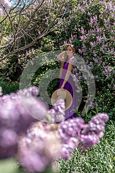 Fashion Model in Lilac Flowers, Young Woman in Beautiful Long Dress Waving on Wind, Outdoor Beauty Portrait in Blooming