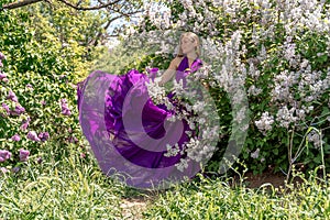 Fashion Model in Lilac Flowers, Young Woman in Beautiful Long Dress Waving on Wind, Outdoor Beauty Portrait in Blooming