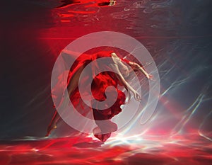 fashion model posing with sexy legs. Fantasy woman dancing under water sea, red long silk dress fabric floating