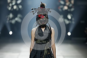 fashion model on a runway wearing avantgarde attire and a kabuki mask