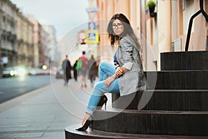 Fashion Model In Street. Beautiful Sexy Woman In Stylish Fashionable Fall Clothes sitting on stairs