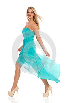 Fashion Model In Turquoise Dress Is Walking And Looking At Camera