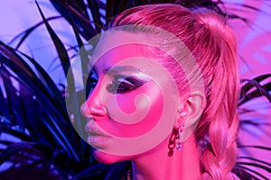 Fashion model woman with a bright make-up in colourful bright neon uv lights posing in studio